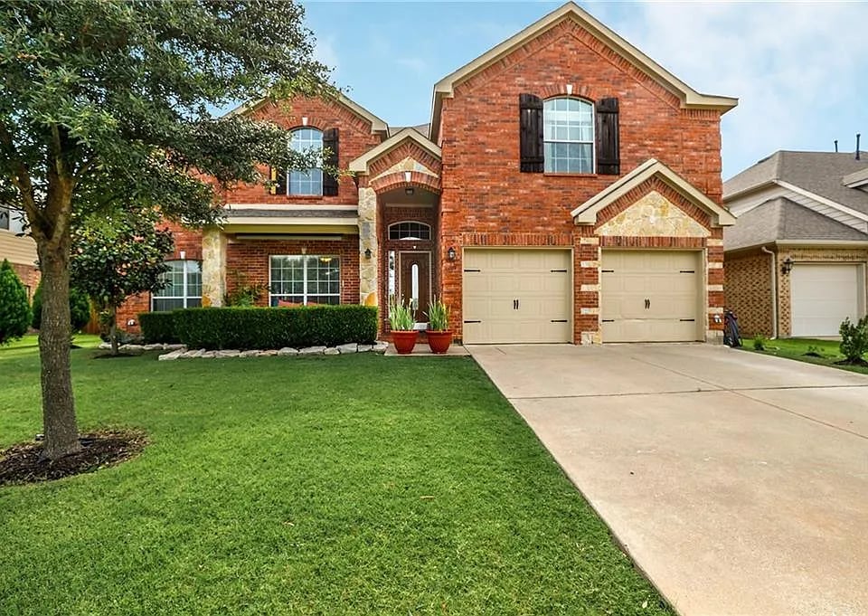 Two-story red brick house with stone accents, a two-car garage, and a wide driveway.