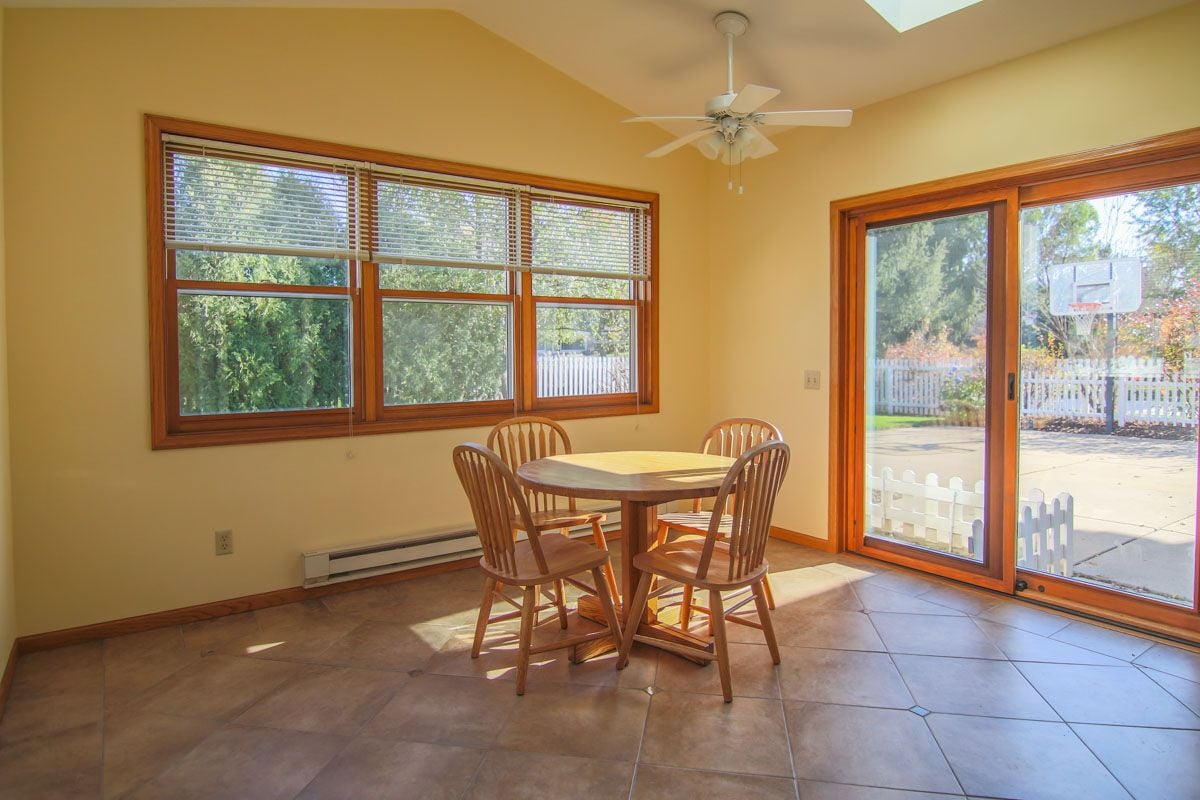 Dining area with a round wooden table beside large windows and sliding glass doors.
