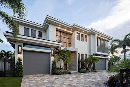 Modern two-story home with a broad paver driveway, two garage doors, and palms by the entrance.