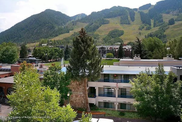 Aspen town buildings and trees below green mountain slopes.