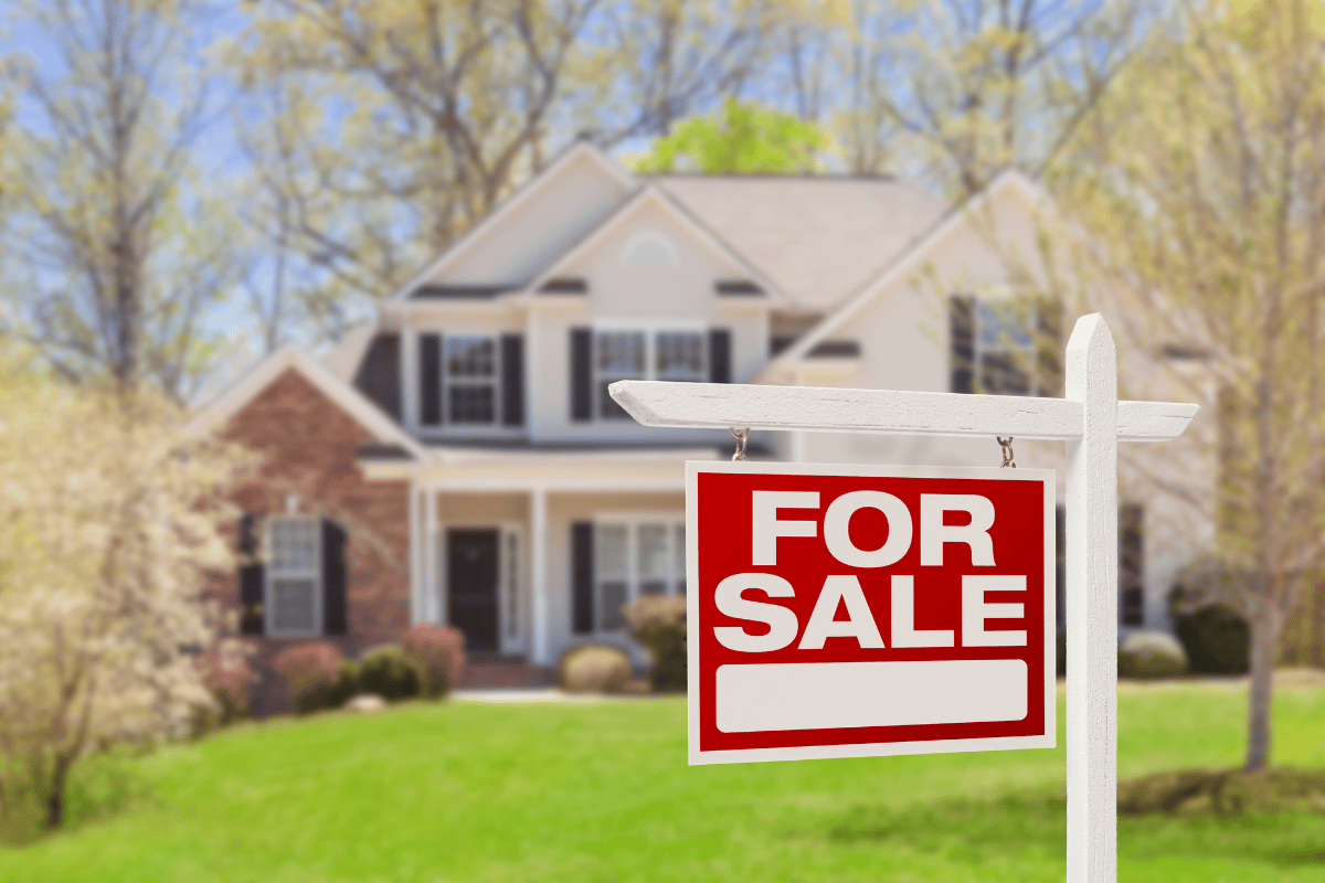 Classic two-story home with a “For Sale” sign on the front lawn during spring, ready for real estate listing.