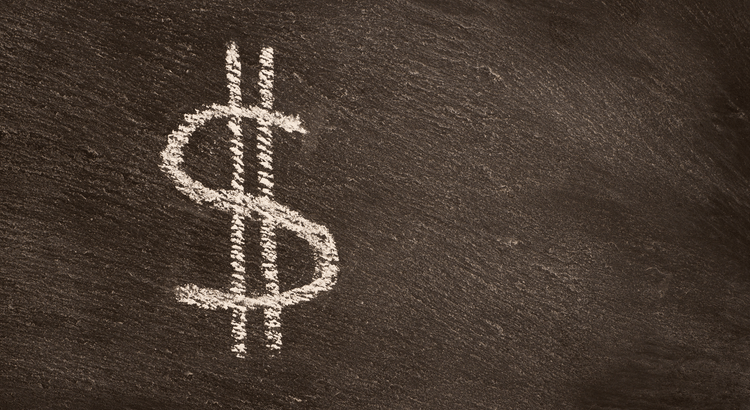 A large white chalk dollar sign is drawn on a dark chalkboard. The texture of the chalkboard adds contrast, conveying themes of finance or education.