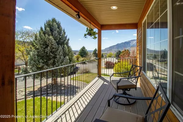 Covered porch with lounge chairs overlooking colorful trees, a landscaped yard, and distant mountains.