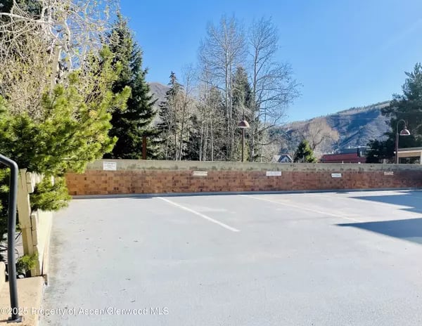 Parking lot with marked spaces, a brick wall, and a mountain slope beyond the trees.