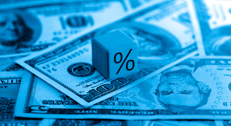 Dollar bills beneath a block marked with a percent symbol, illustrating mortgage rates.