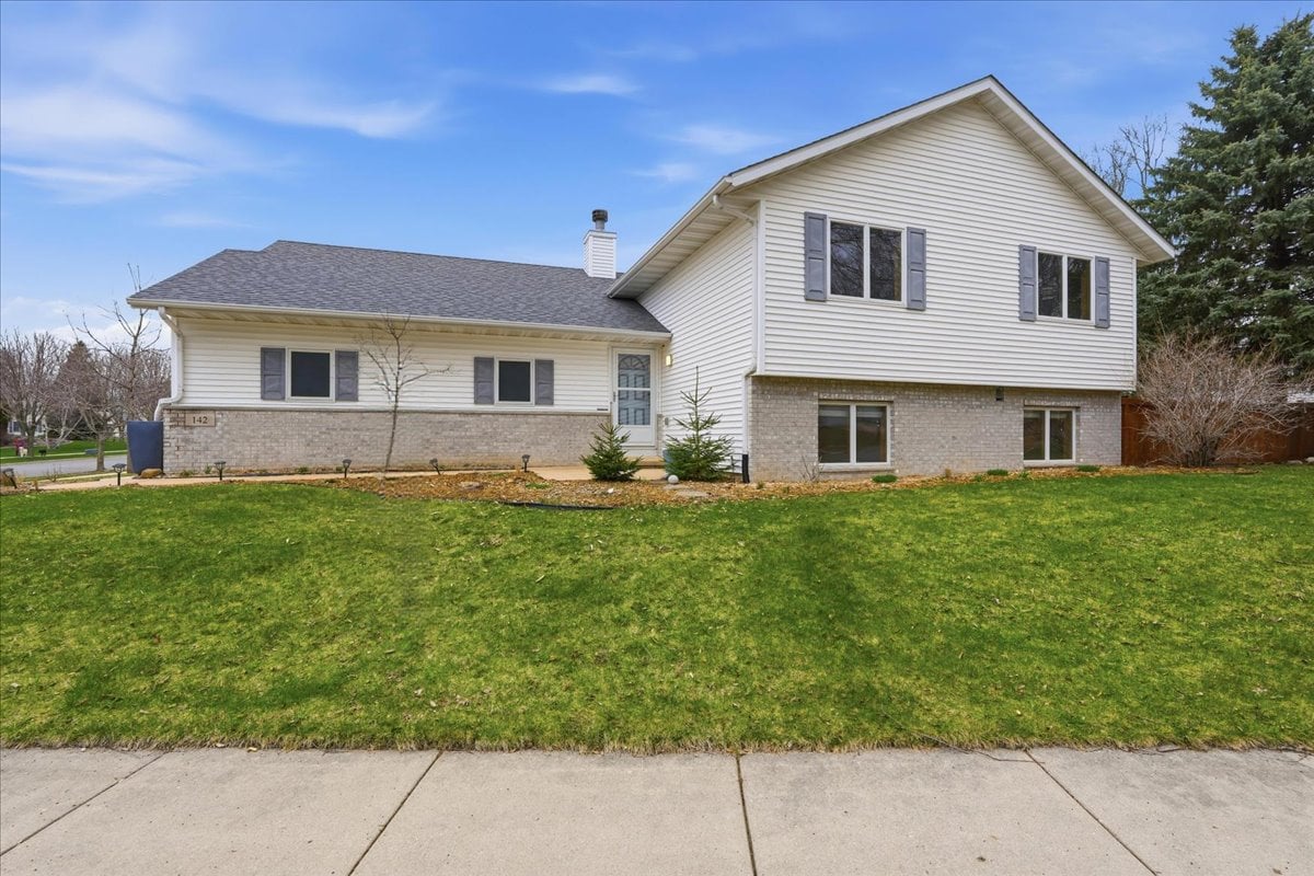 A bright, front-facing exterior shot of 142 Meadow Ridge Lane, showing the white siding, brick accents, and large corner lot on Madison's Northside.