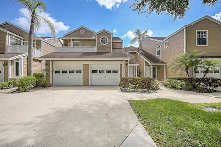 Two-story tan home with a two-car garage, broad driveway, and palm trees.