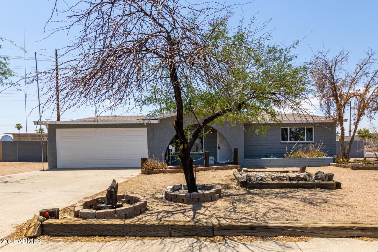 Gray single-story home with a white double garage and a large tree in the dry front yard.