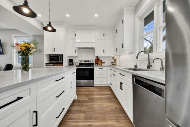 White kitchen with a large island, stainless-steel appliances, and wood-look flooring.
