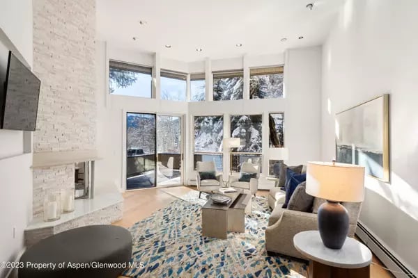 Living room with a white stone fireplace, tall windows, and contemporary seating.