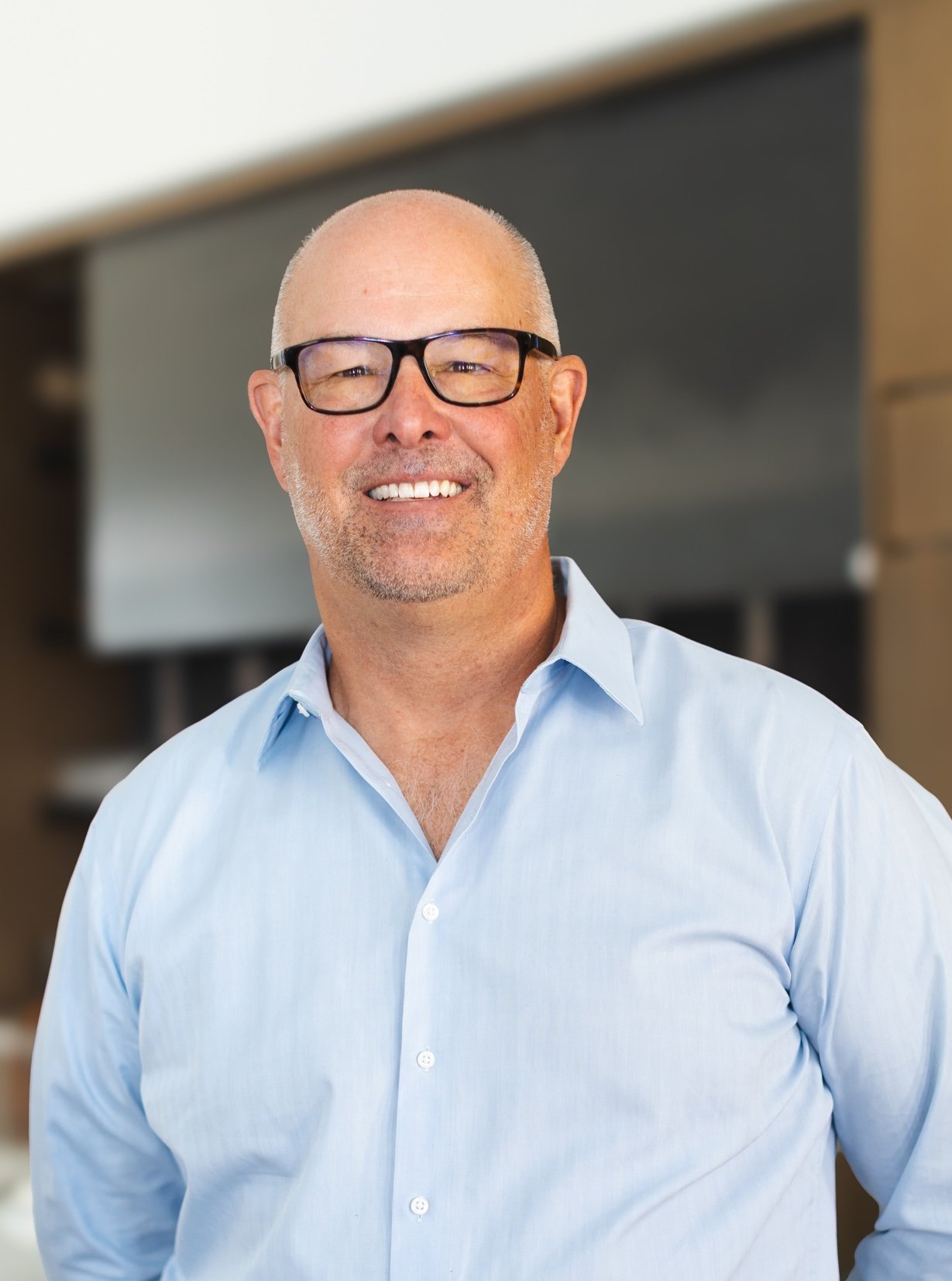 Daniel Zemke smiling in black glasses and a light blue button-down shirt.