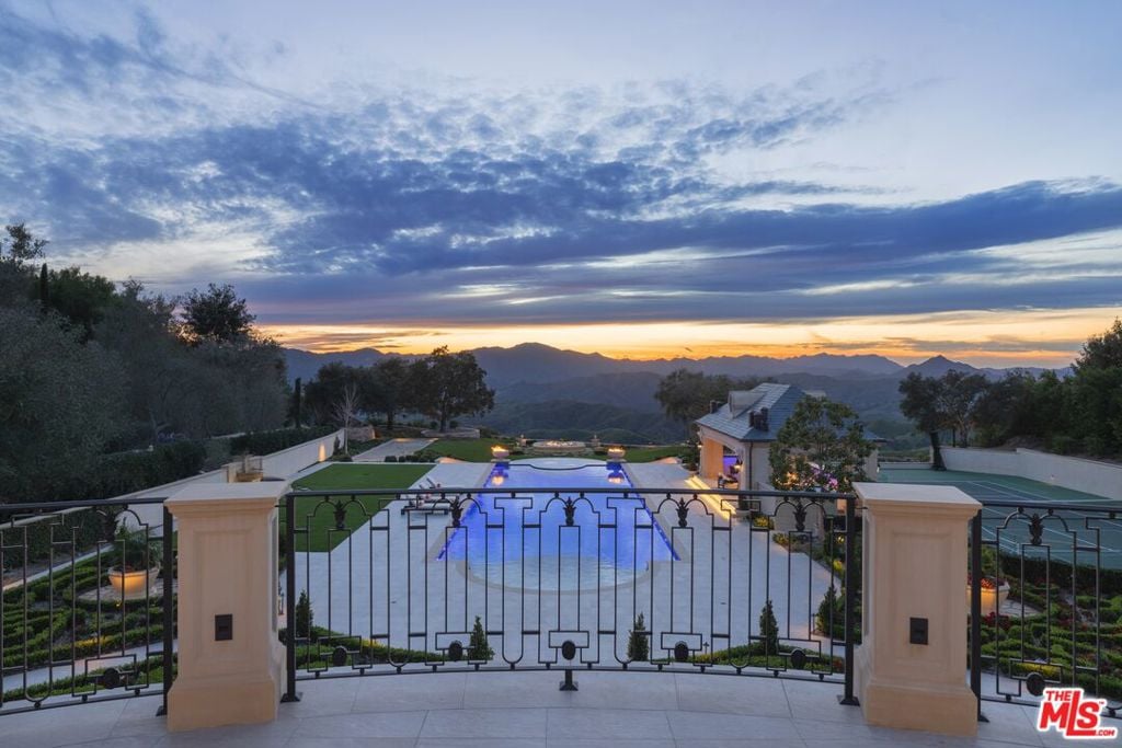 Estate pool and landscaped grounds behind a wrought-iron gate, with mountains at dusk.