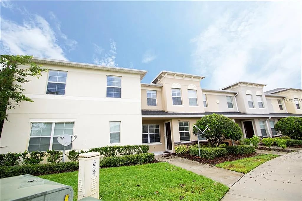 Two-story attached townhomes with light facades, landscaped lawns, and a sidewalk.