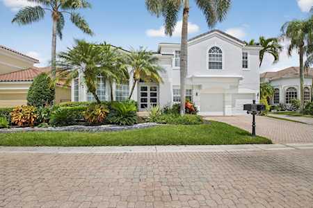Two-story white house with an arched window, paved driveway, tropical landscaping, and palm trees.