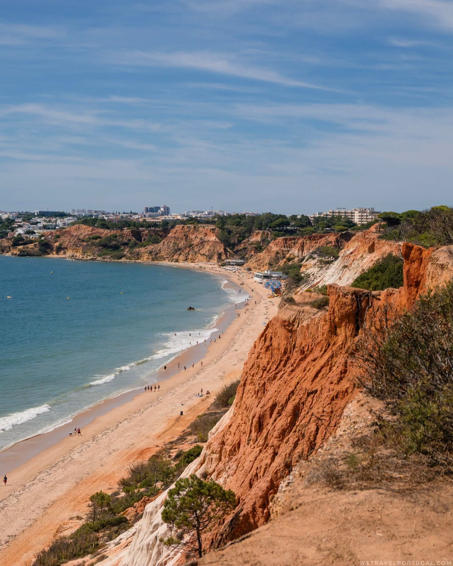 The long sweep of Praia da Falesia curving into the distance beneath red sandstone cliffs, with the town on the horizon