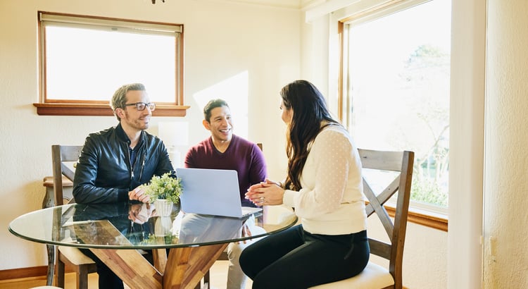 Three adults talking around a glass table, with a laptop and flowers.