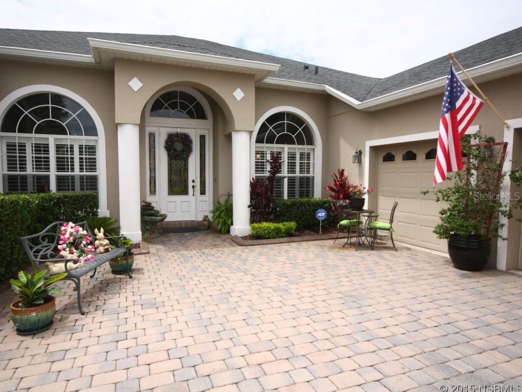 Home exterior with arched windows, a paved courtyard, patio seating, and an American flag.