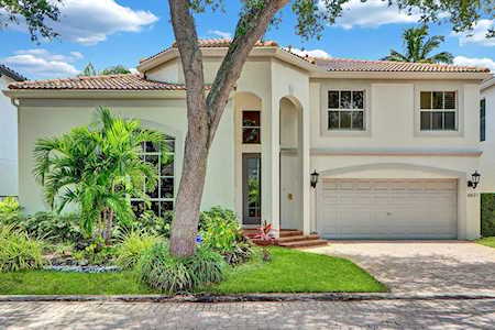 Two-story home with a tiled roof, arched entry, attached garage, and tropical landscaping.