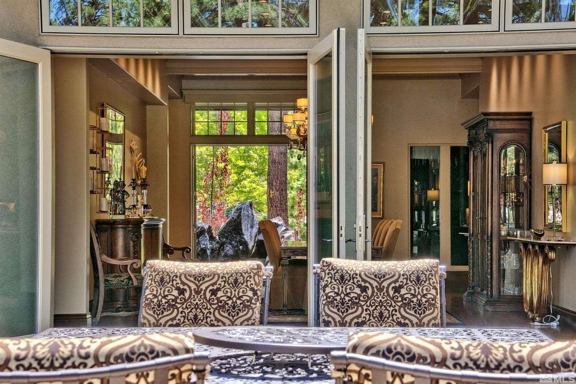Dining room with patterned chairs, tall windows, and open glass doors facing a garden.