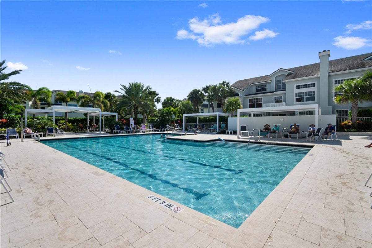 Condominium swimming pool with a broad tiled deck, lounge chairs, and palm trees.
