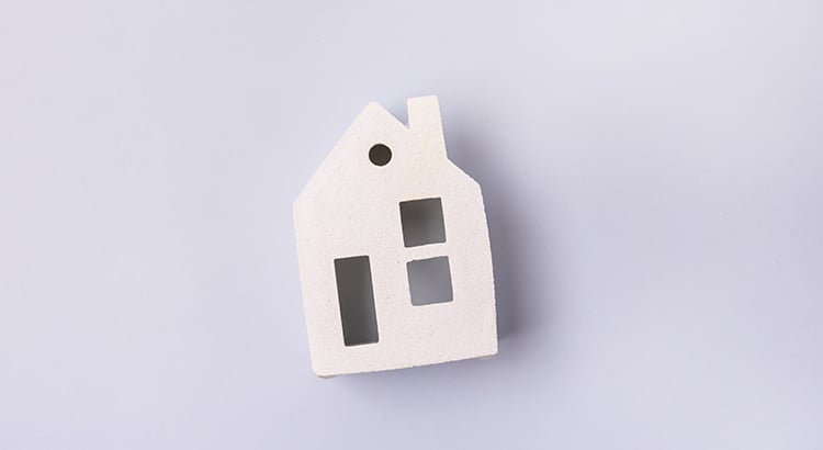 White house-shaped object with cutout windows on a pale lavender surface.