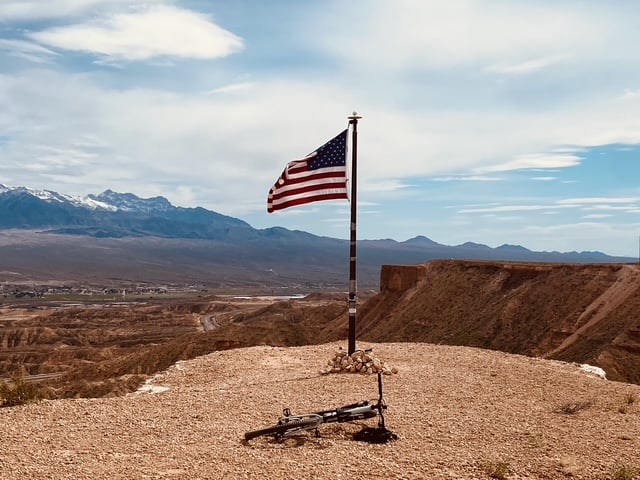U.S. flag on a rocky ridge overlooking a desert valley and distant mountains.