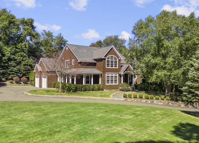 Two-story brick house with a gabled roof, attached garage, curved driveway, and broad green lawn.