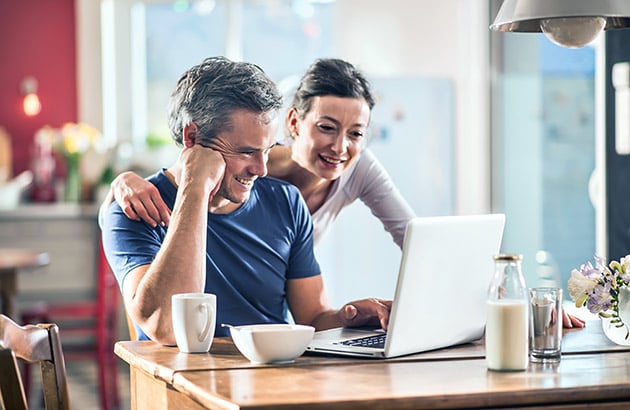 A couple looks at a laptop together at a bright kitchen counter.