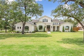White home with a covered entry, broad green lawn, and mature trees.