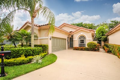 Peach stucco home with a tile roof, arched window, palm trees, and a curved driveway.