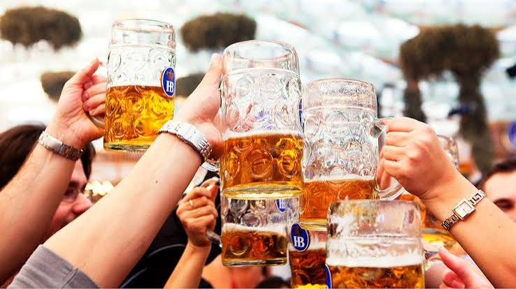 People clink large beer steins filled with amber beer at an outdoor celebration.
