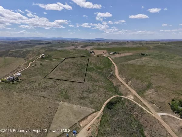 Aerial view of a marked rural parcel amid rolling terrain and dirt roads.