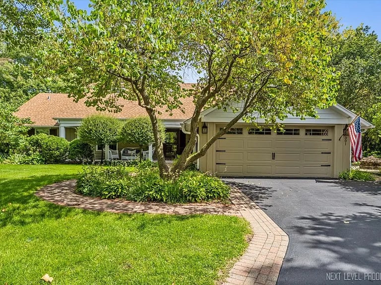 Single-story home with a two-car garage, mature trees, and a curved brick walkway.
