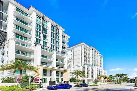 Modern white condominium buildings with glass balconies, palm trees, and parked cars along the street.