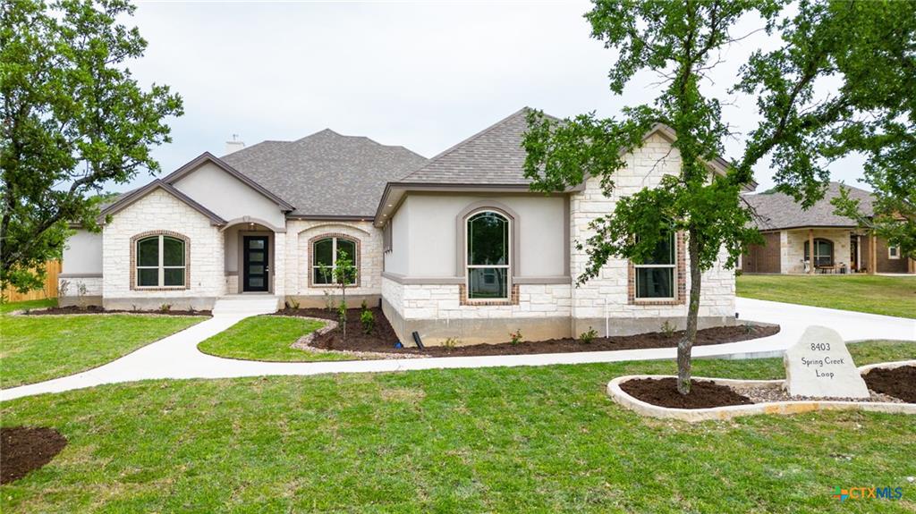 Single-story stone-and-stucco home with arched windows and a Spring Creek Loop address marker.