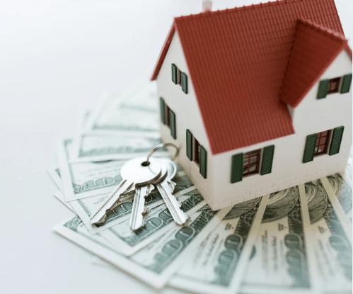 Model house and keys resting on dollar bills.