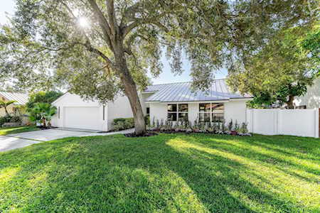 Single-story home with a light metal roof, a mature shade tree, and a broad green lawn.
