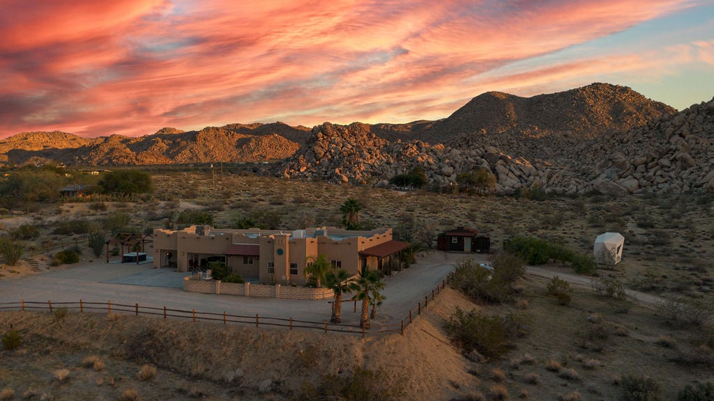 Desert home beneath rocky mountains and a vivid sunset sky.