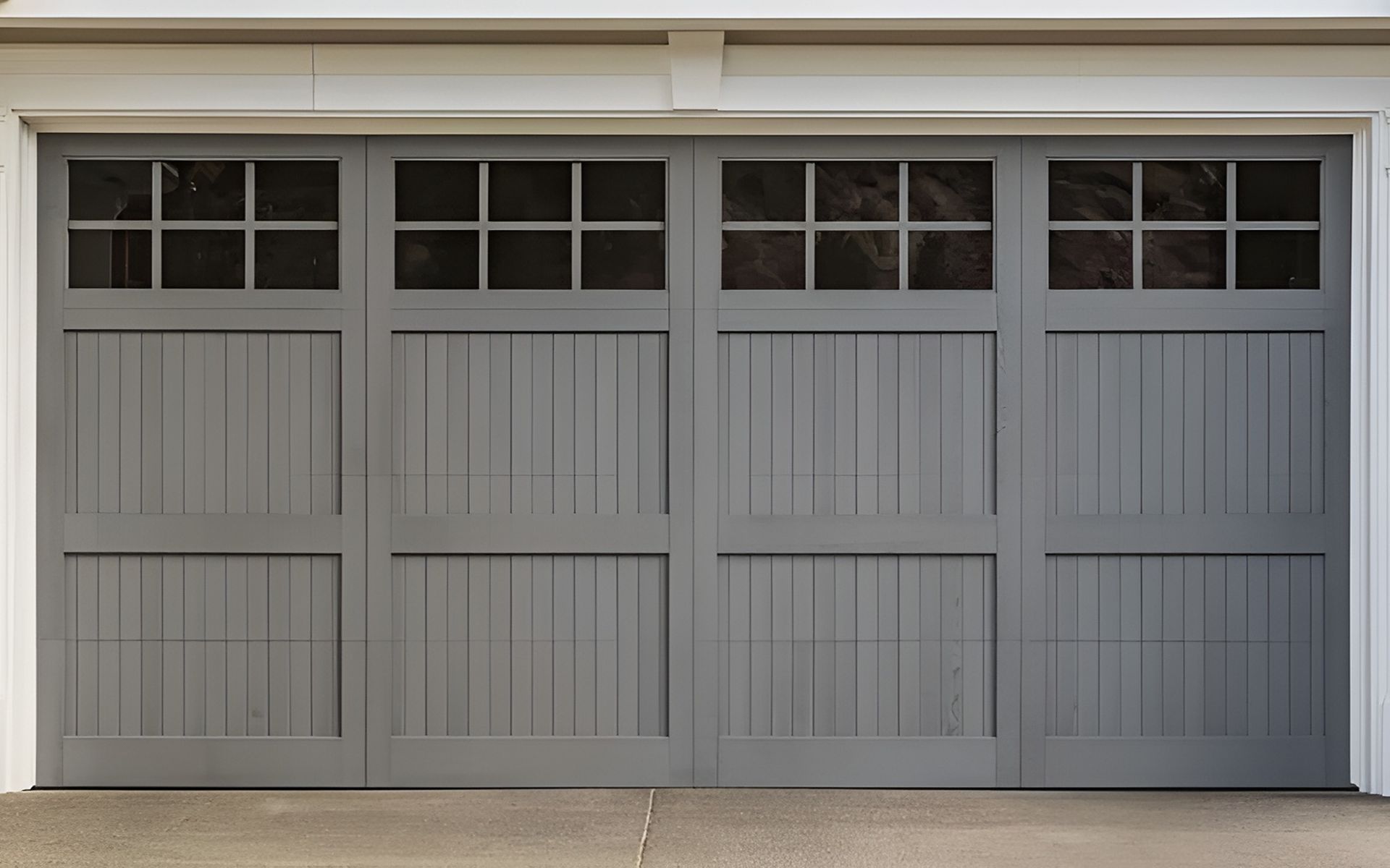 Four gray carriage-style garage doors with gridded windows and vertical panels.