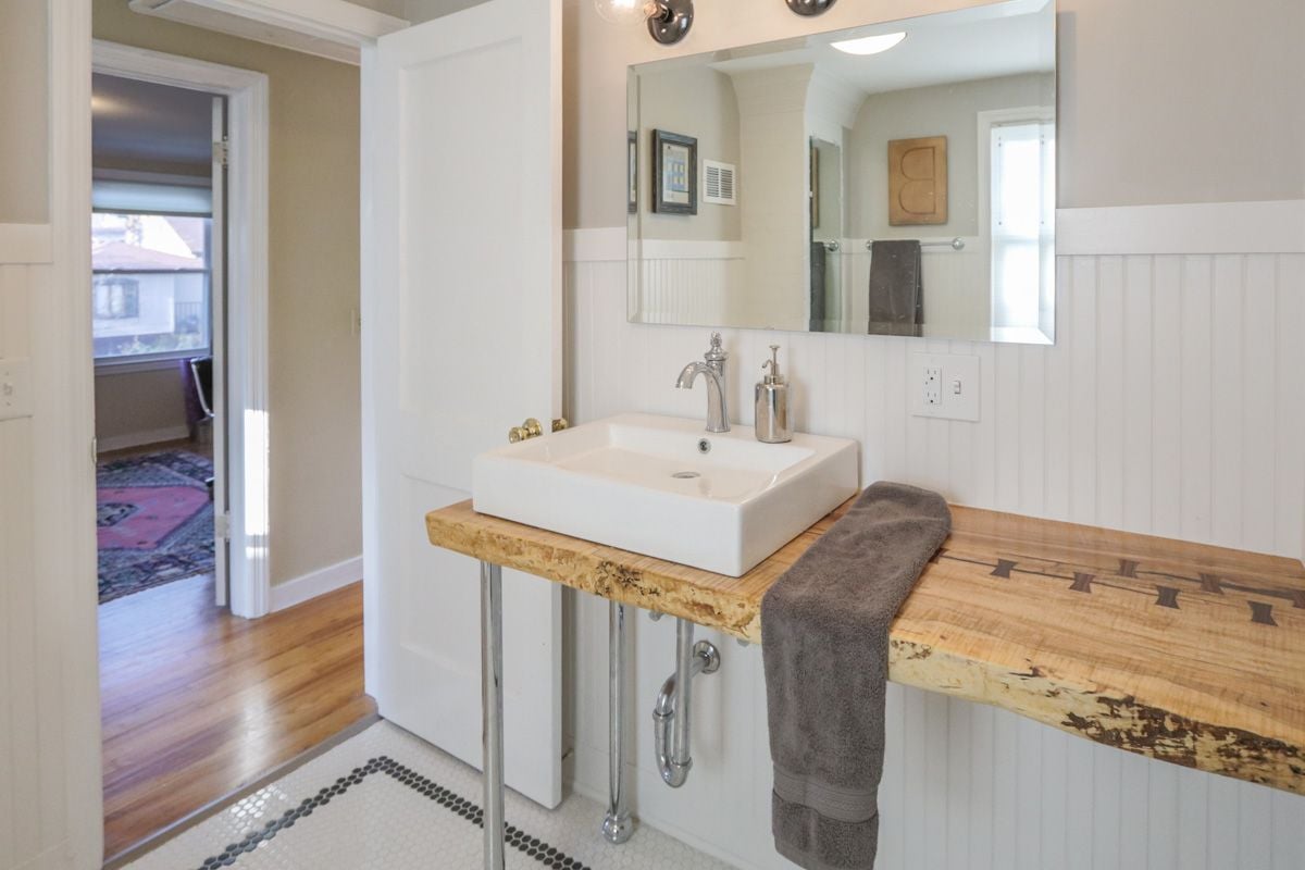 Bathroom with a vessel sink on a rustic wood counter and white beadboard walls.