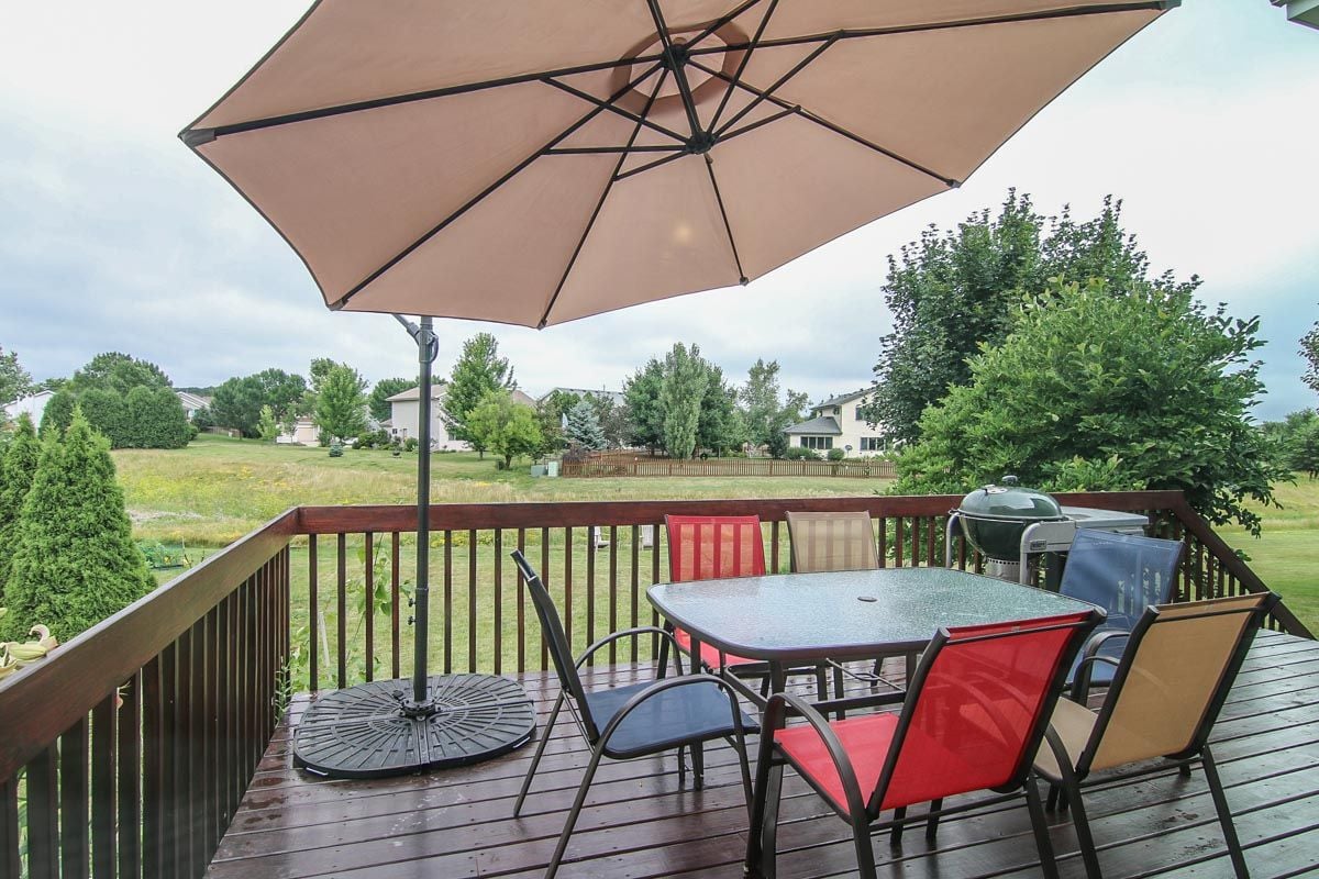 Wooden deck with umbrella-shaded dining set and grill overlooking a grassy yard.