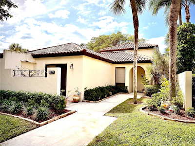Cream stucco home with a tiled roof, curved walkway, and palm trees in the front yard.
