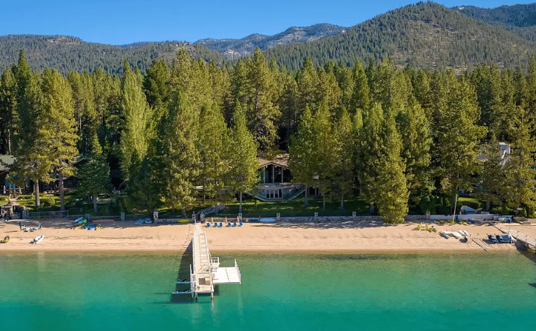 Lakefront beach and dock bordered by trees, with forested mountains beyond.