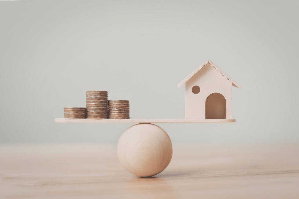 Balanced seesaw with coins and house symbolizing real estate investment.