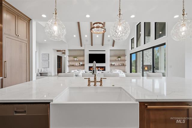 Luxury kitchen with a large white island, brass fixtures, and a vaulted living room beyond.