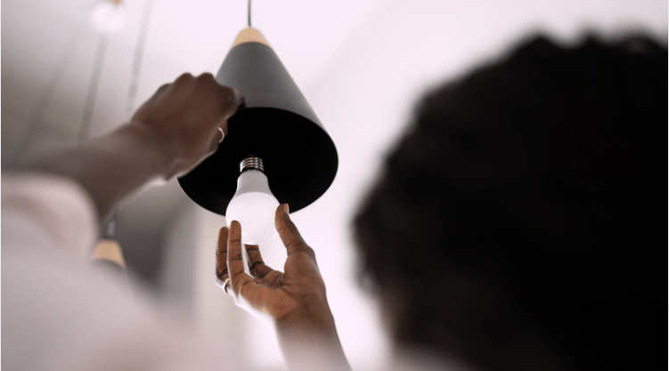 A person replaces a bulb in a black pendant ceiling light.