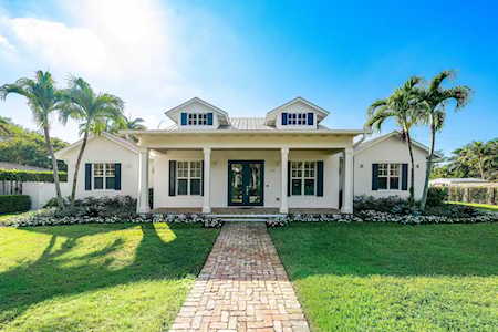 White single-story home with palm trees and a brick walkway across the lawn.