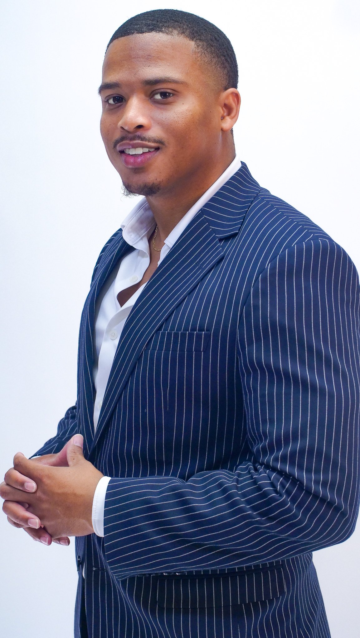 Tafari Witter in a navy pinstripe suit with his hands clasped.