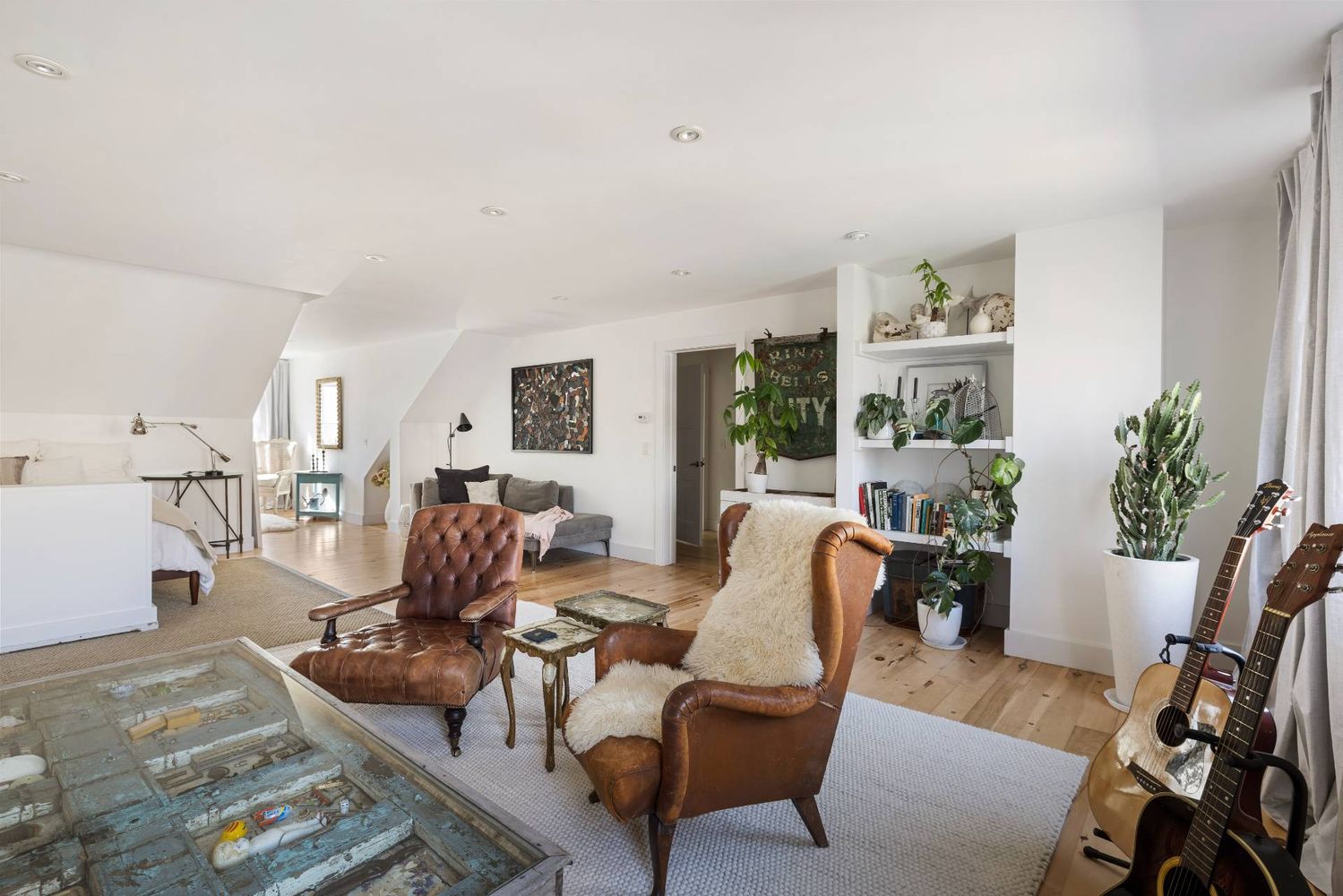 Furnished loft living room with sloped ceilings, leather chairs, built-in shelves, and guitars.