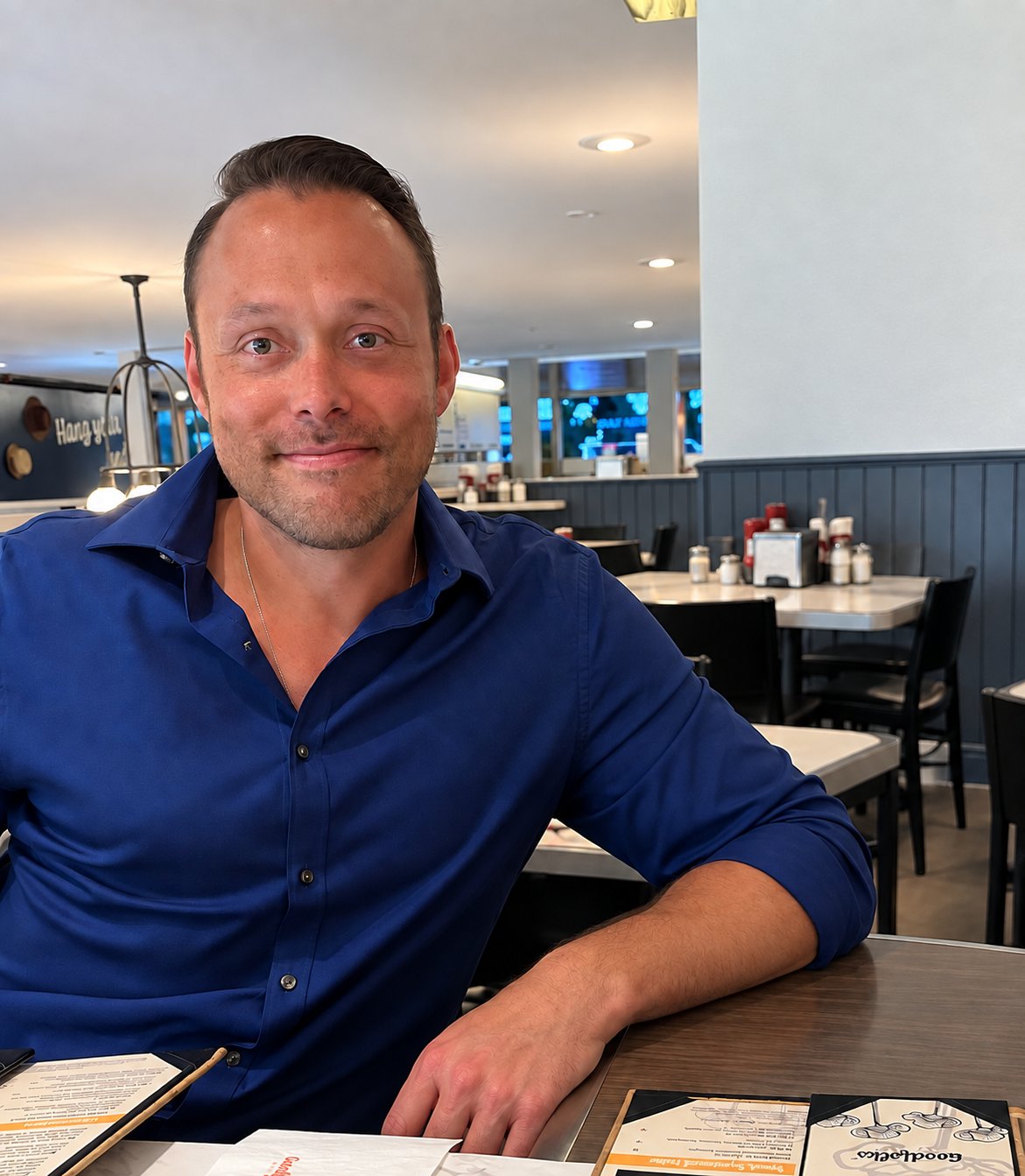Man in a blue shirt seated at a restaurant table with menus.